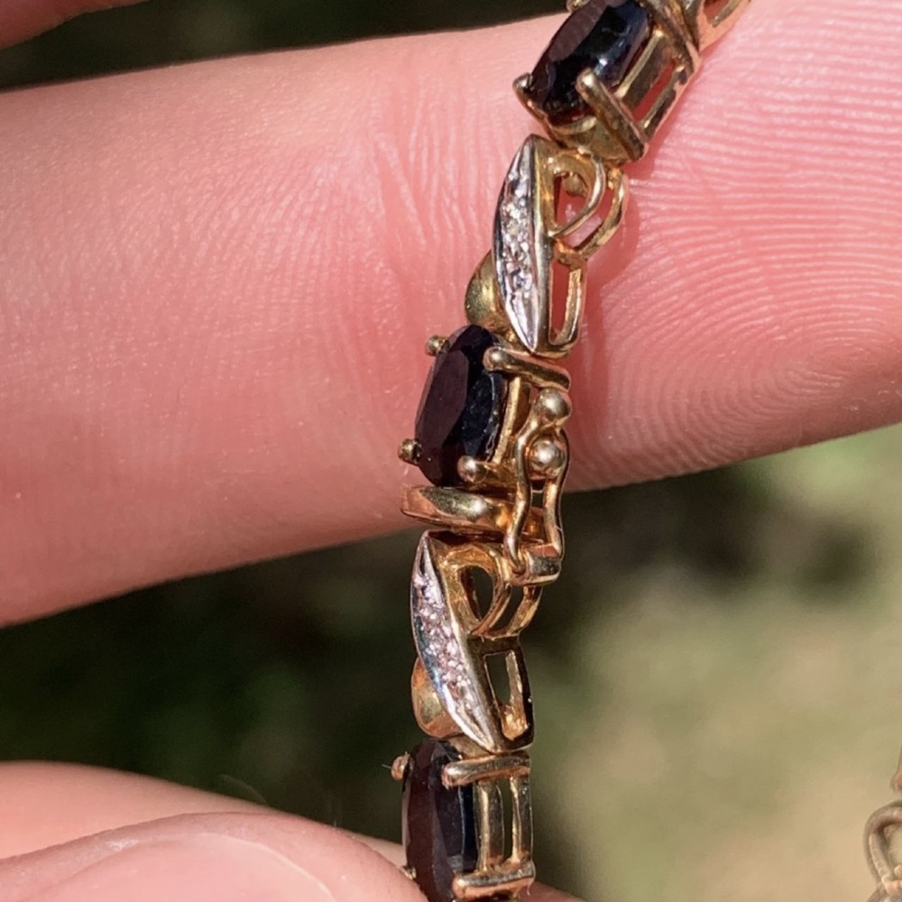 A 9ct yellow gold link bracelet set with oval-cut dark blue sapphires and accent diamond links, worn on a wrist. View VIII