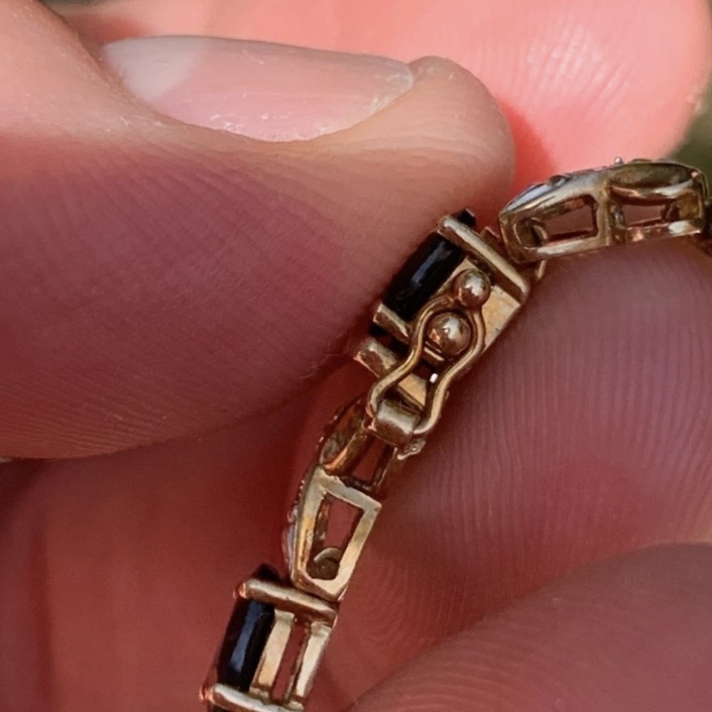 A 9ct yellow gold link bracelet set with oval-cut dark blue sapphires and accent diamond links, worn on a wrist. View IX