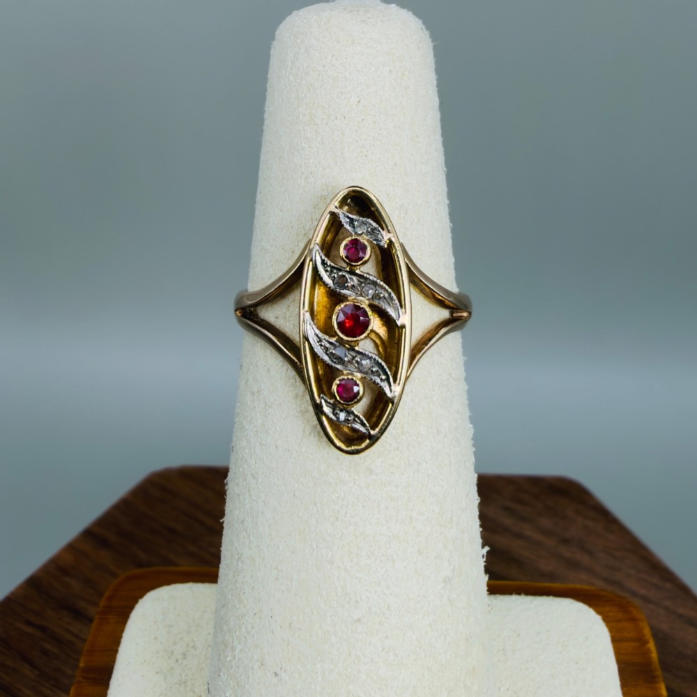 An 18ct gold Art Nouveau navette ring featuring three round rubies set within an openwork marquise-shaped mount detailed with diamonds. View V