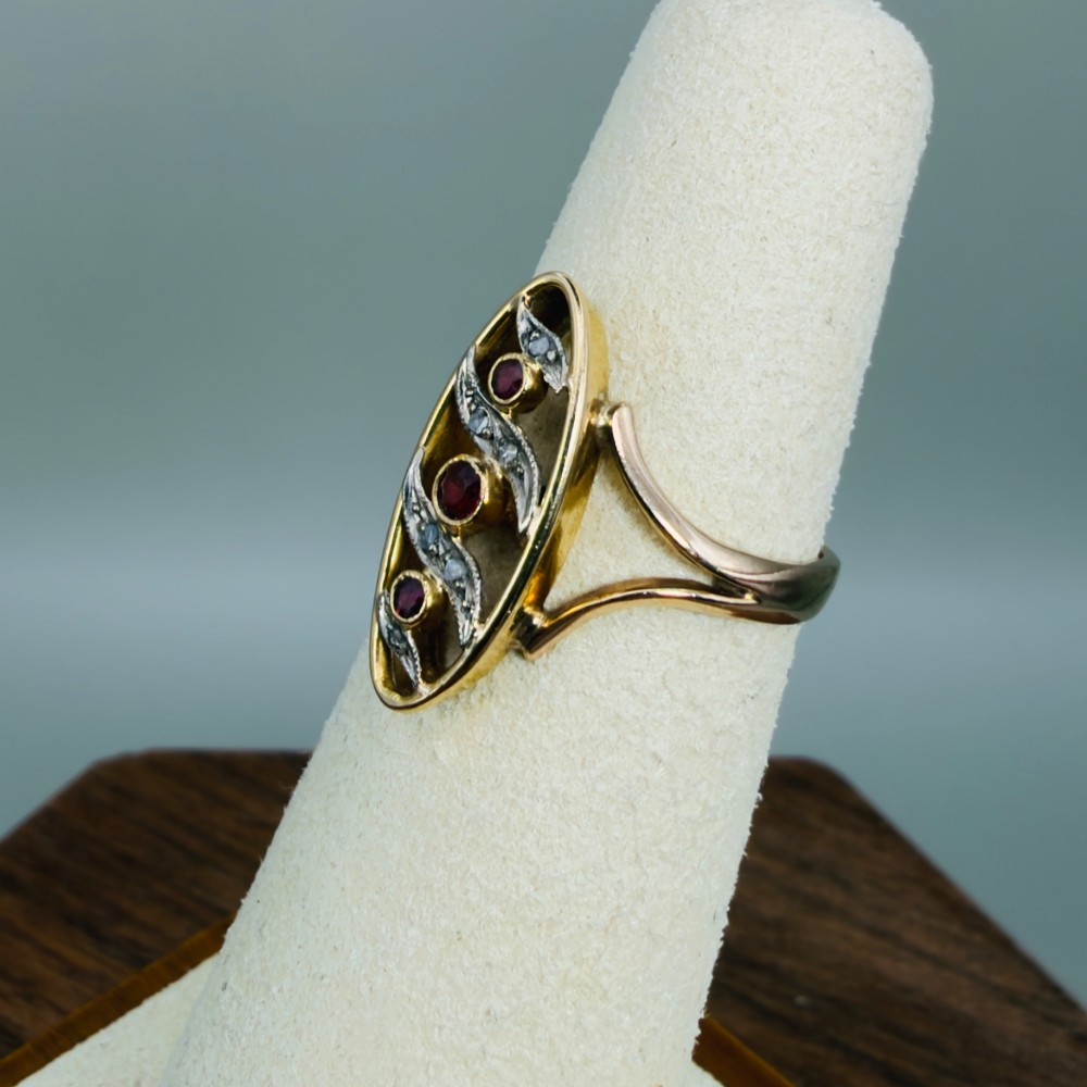 An 18ct gold Art Nouveau navette ring featuring three round rubies set within an openwork marquise-shaped mount detailed with diamonds. View VI