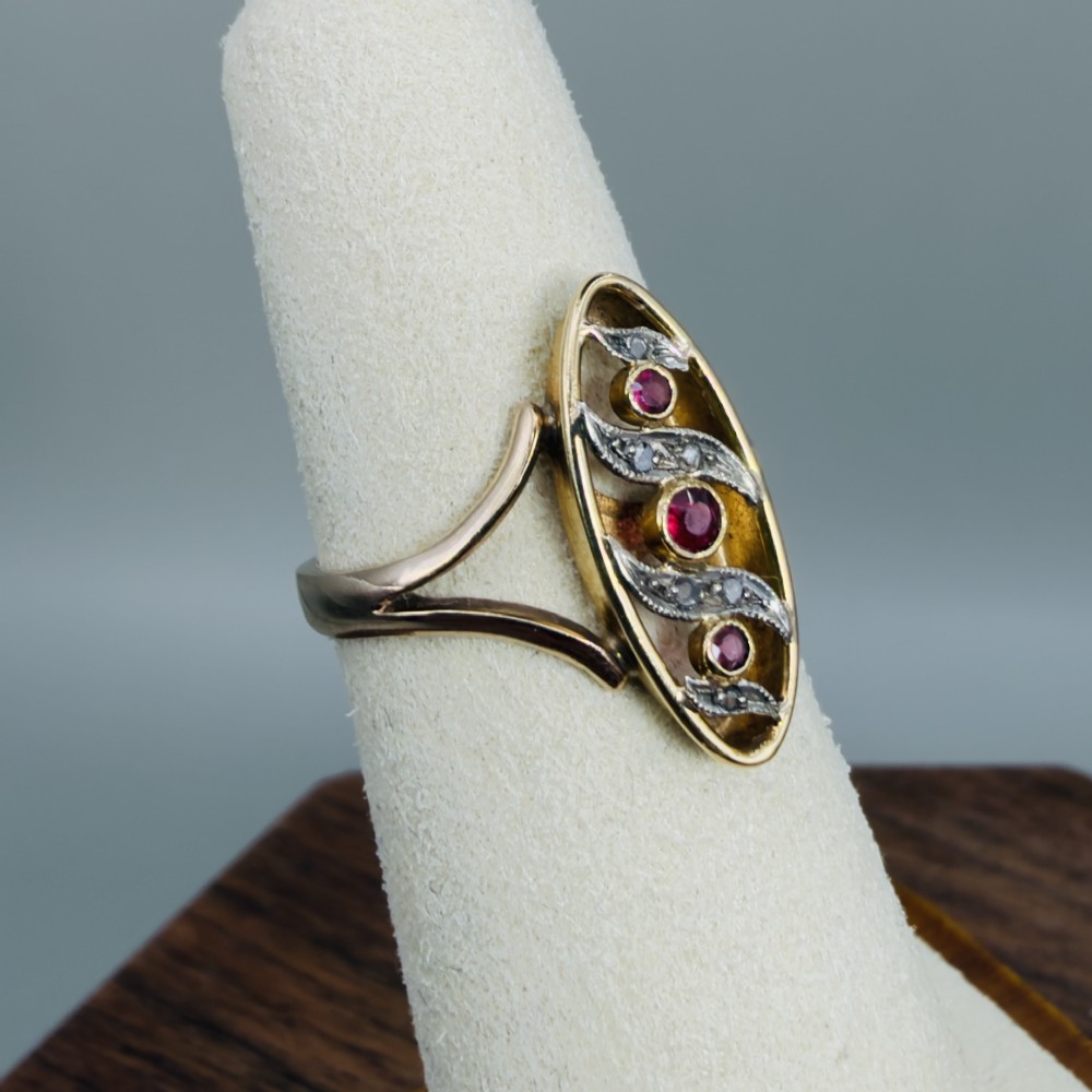 An 18ct gold Art Nouveau navette ring featuring three round rubies set within an openwork marquise-shaped mount detailed with diamonds. View VII