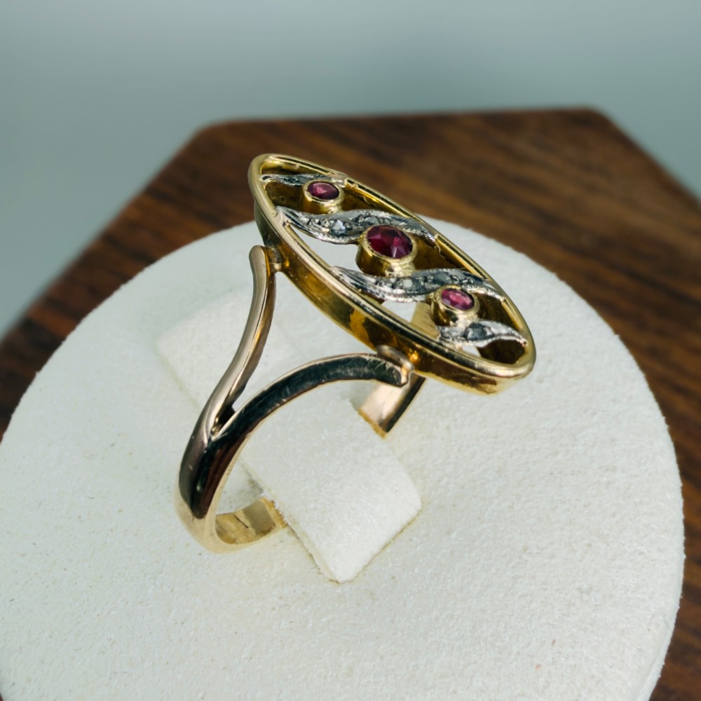 An 18ct gold Art Nouveau navette ring featuring three round rubies set within an openwork marquise-shaped mount detailed with diamonds. View IX