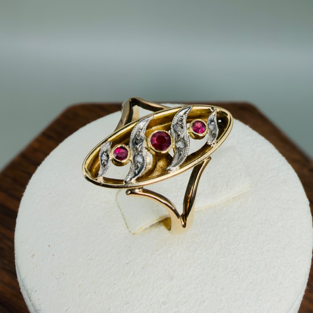 An 18ct gold Art Nouveau navette ring featuring three round rubies set within an openwork marquise-shaped mount detailed with diamonds. View X