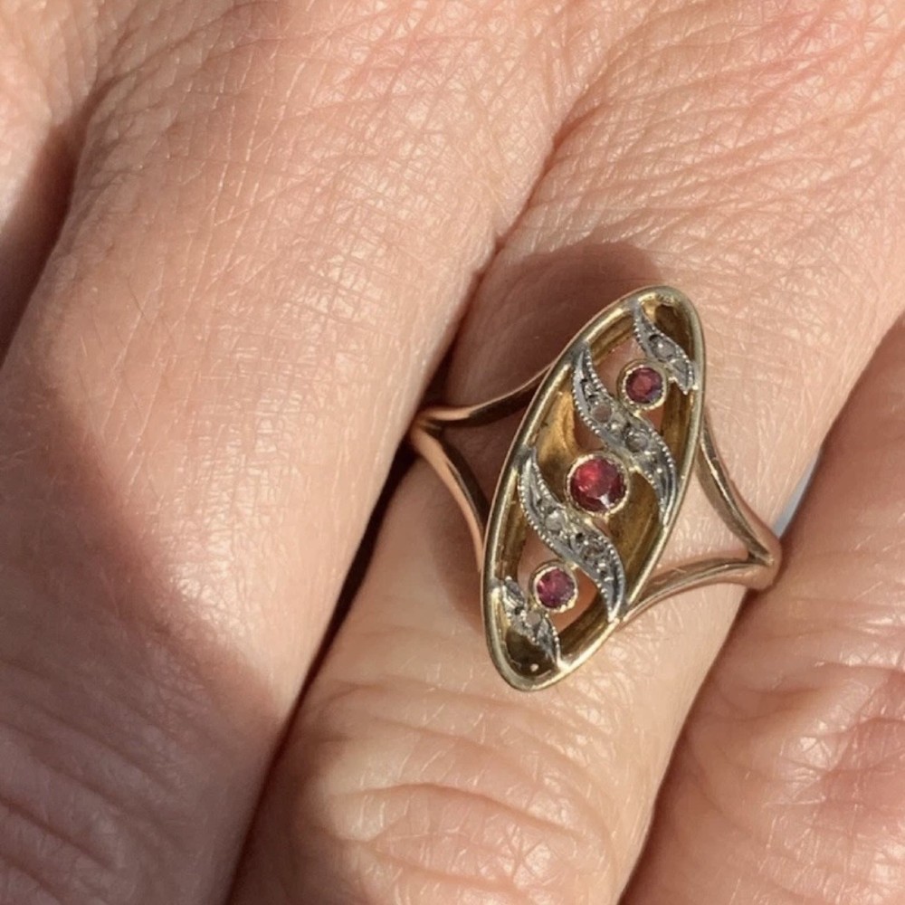 An 18ct gold Art Nouveau navette ring featuring three round rubies set within an openwork marquise-shaped mount detailed with diamonds. View XI