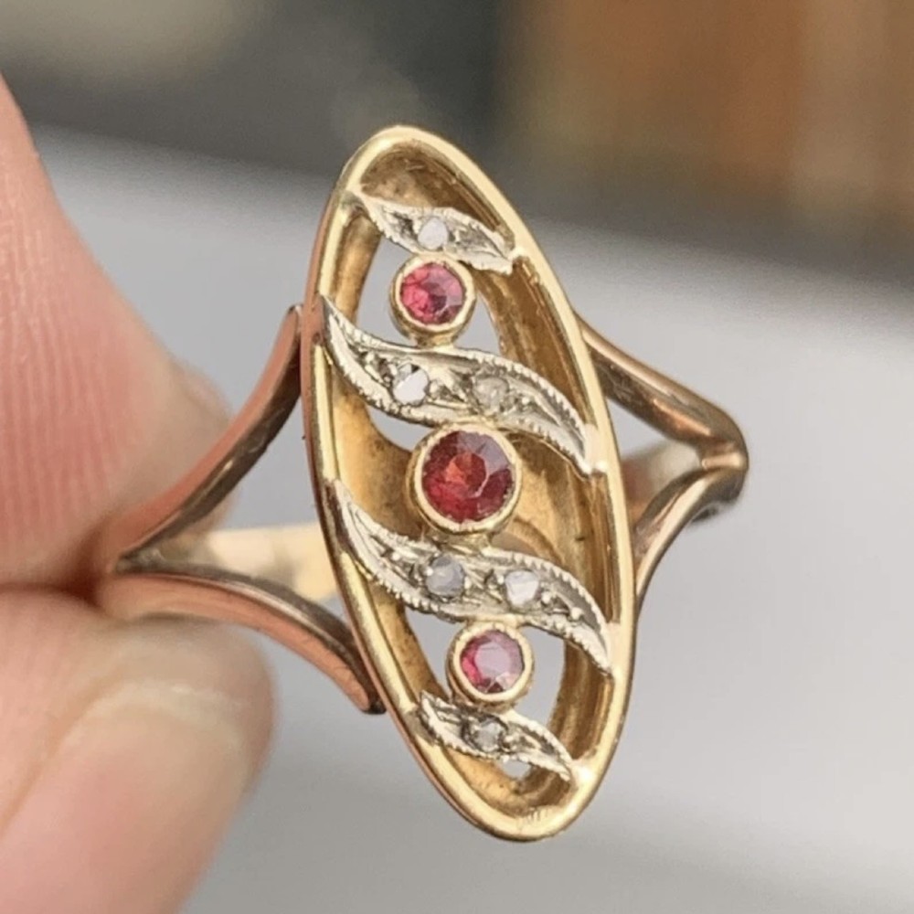 An 18ct gold Art Nouveau navette ring featuring three round rubies set within an openwork marquise-shaped mount detailed with diamonds. View XII