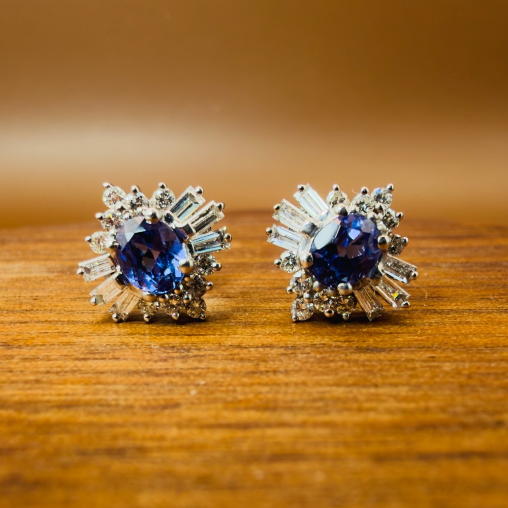 A pair of 18ct white gold cluster earrings featuring central oval cornflower blue sapphires framed by round and baguette-cut diamonds. View VI