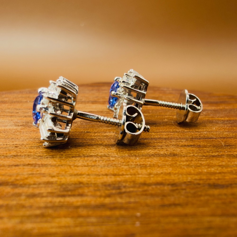 A pair of 18ct white gold cluster earrings featuring central oval cornflower blue sapphires framed by round and baguette-cut diamonds. View VII