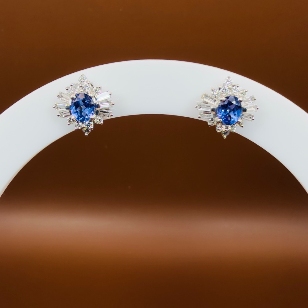 A pair of 18ct white gold cluster earrings featuring central oval cornflower blue sapphires framed by round and baguette-cut diamonds. View VIII