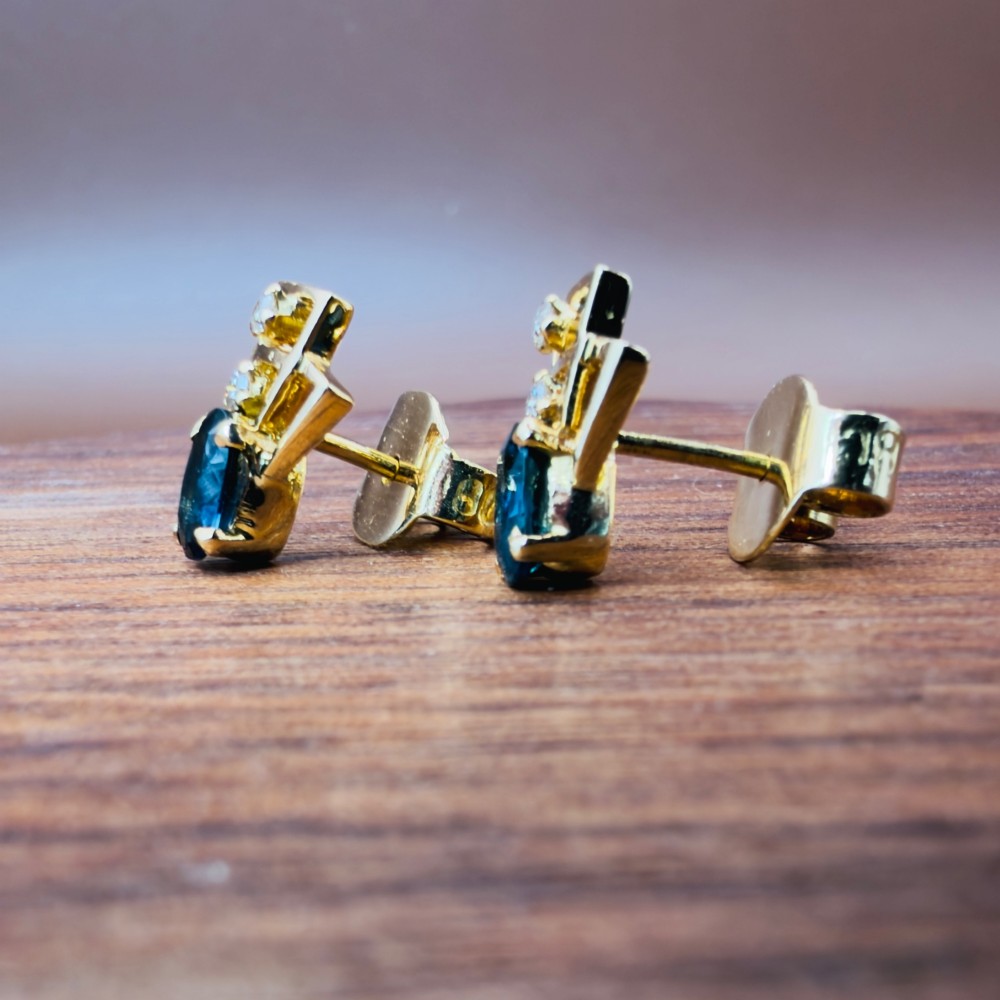A pair of 18ct yellow gold Art Deco stud earrings featuring an oval blue sapphire topped with two round diamonds inside a geometric openwork frame. View VII