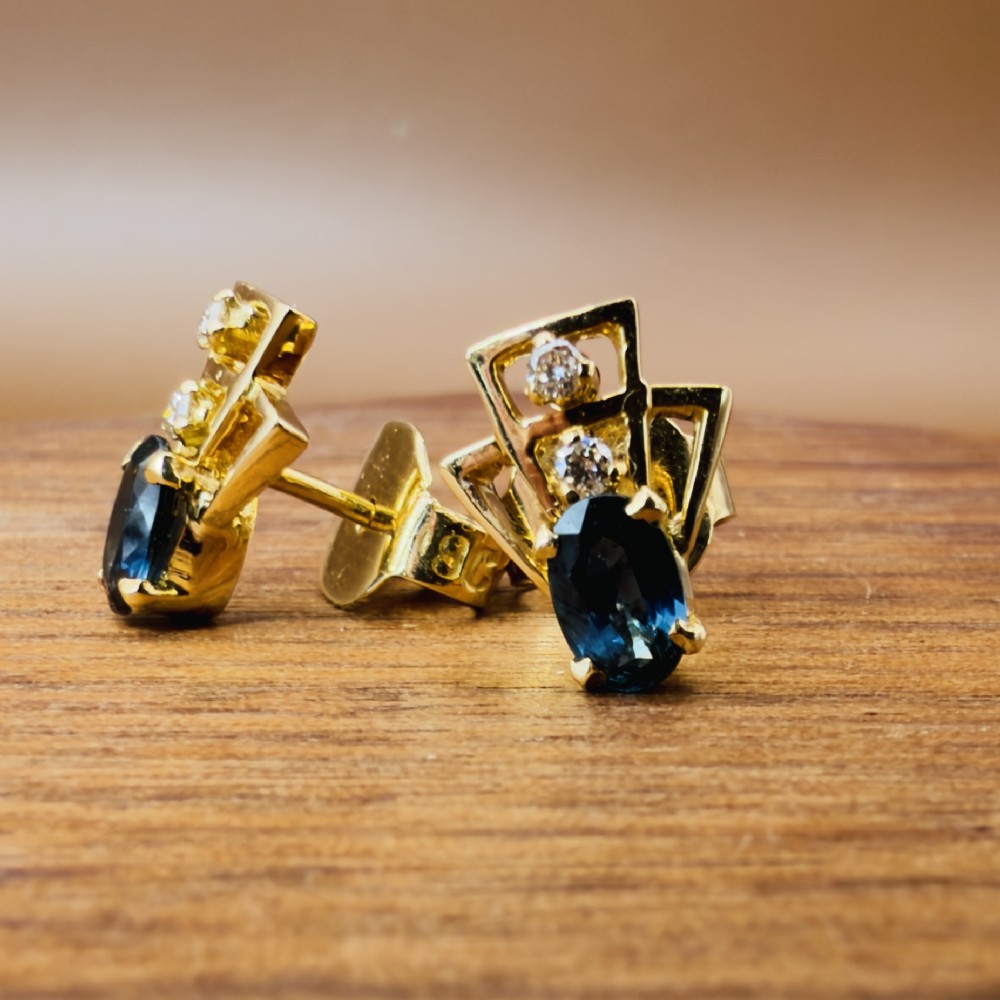 A pair of 18ct yellow gold Art Deco stud earrings featuring an oval blue sapphire topped with two round diamonds inside a geometric openwork frame. View VIII