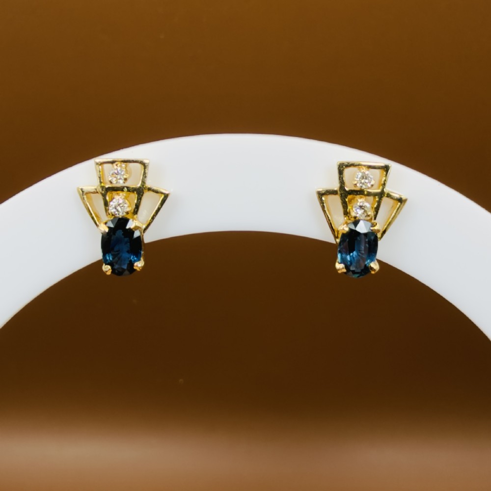 A pair of 18ct yellow gold Art Deco stud earrings featuring an oval blue sapphire topped with two round diamonds inside a geometric openwork frame. View IX