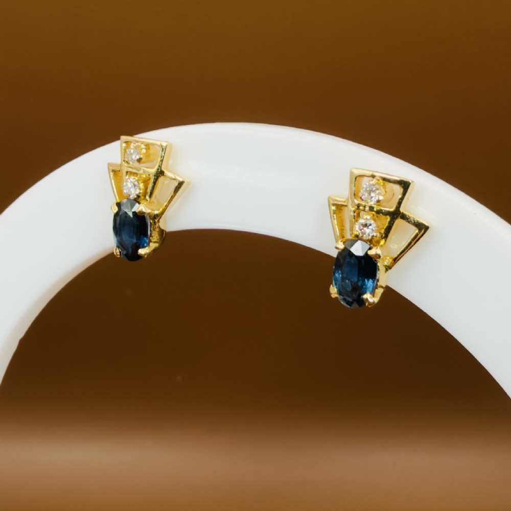 A pair of 18ct yellow gold Art Deco stud earrings featuring an oval blue sapphire topped with two round diamonds inside a geometric openwork frame. View X