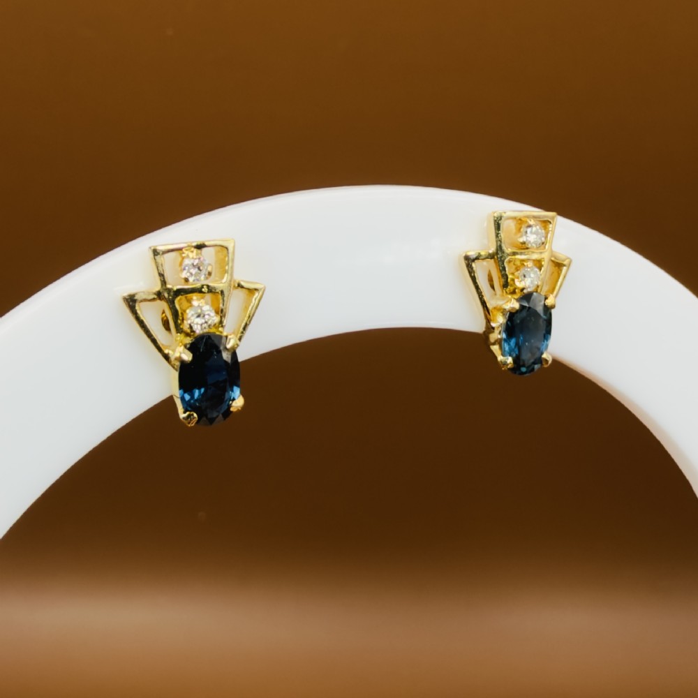 A pair of 18ct yellow gold Art Deco stud earrings featuring an oval blue sapphire topped with two round diamonds inside a geometric openwork frame. View XI