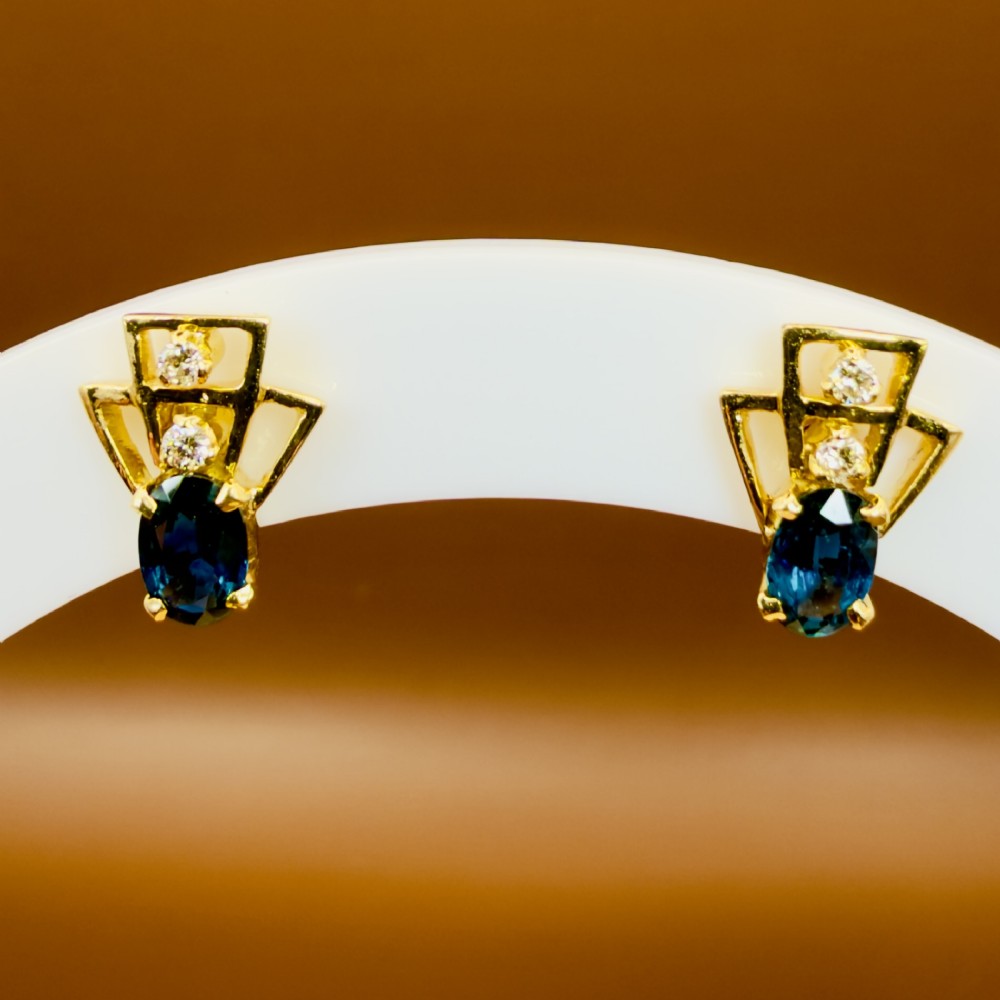 A pair of 18ct yellow gold Art Deco stud earrings featuring an oval blue sapphire topped with two round diamonds inside a geometric openwork frame. View XII