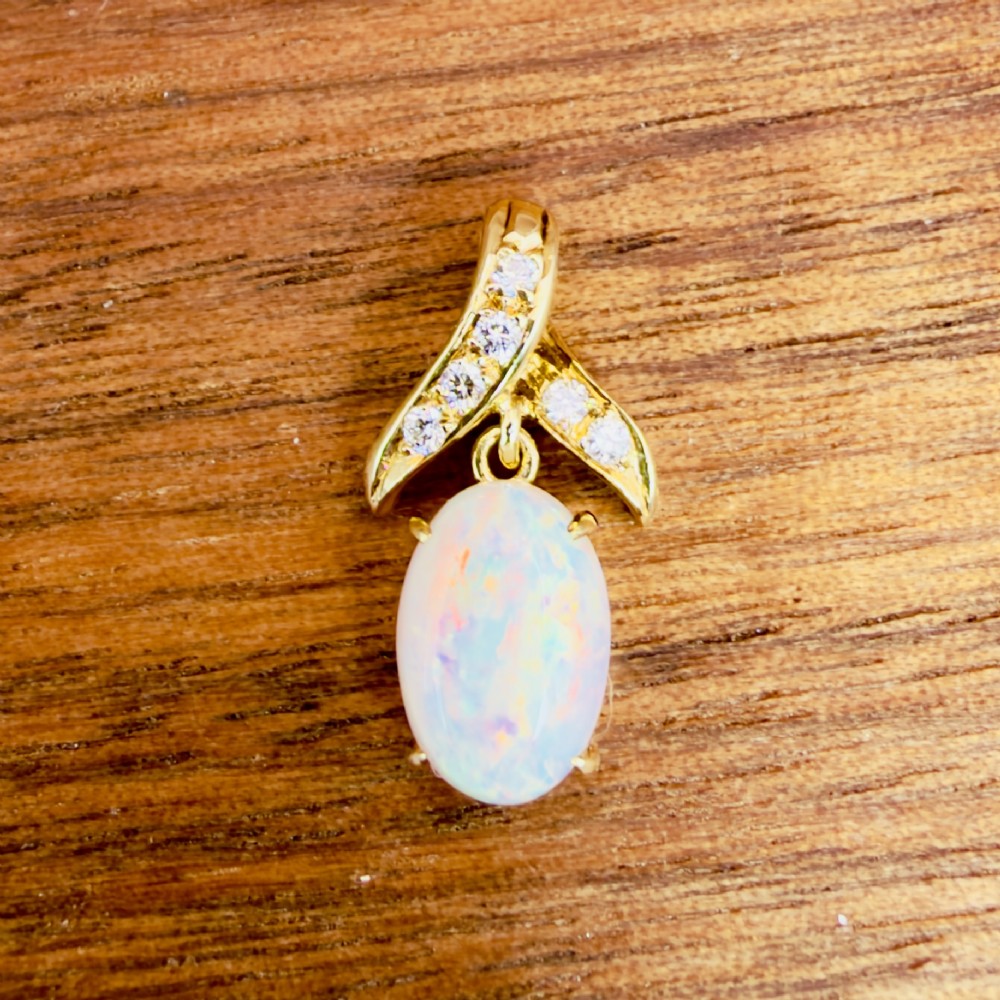 A 14ct yellow gold pendant featuring a claw-set cabochon opal hanging beneath a diamond-accented bail. View II