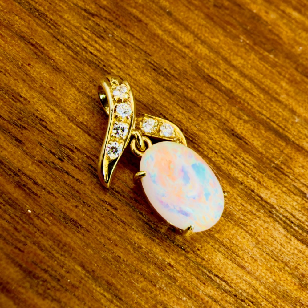A 14ct yellow gold pendant featuring a claw-set cabochon opal hanging beneath a diamond-accented bail. View IV