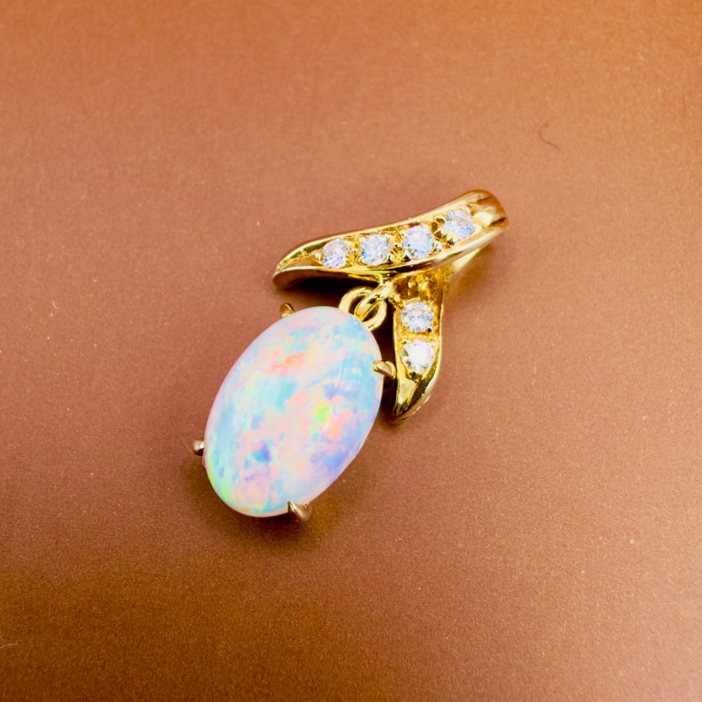 A 14ct yellow gold pendant featuring a claw-set cabochon opal hanging beneath a diamond-accented bail. View V
