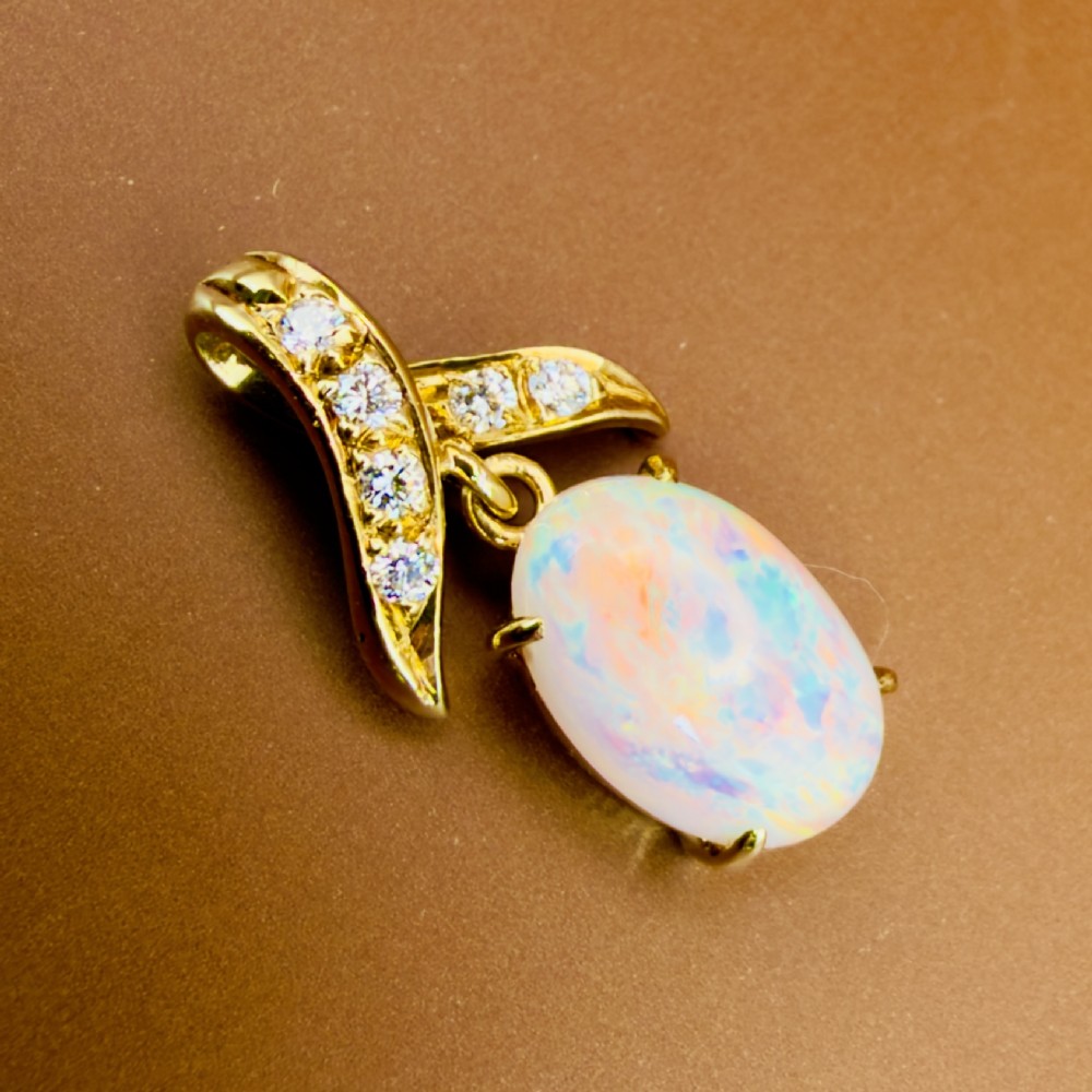 A 14ct yellow gold pendant featuring a claw-set cabochon opal hanging beneath a diamond-accented bail. View VI