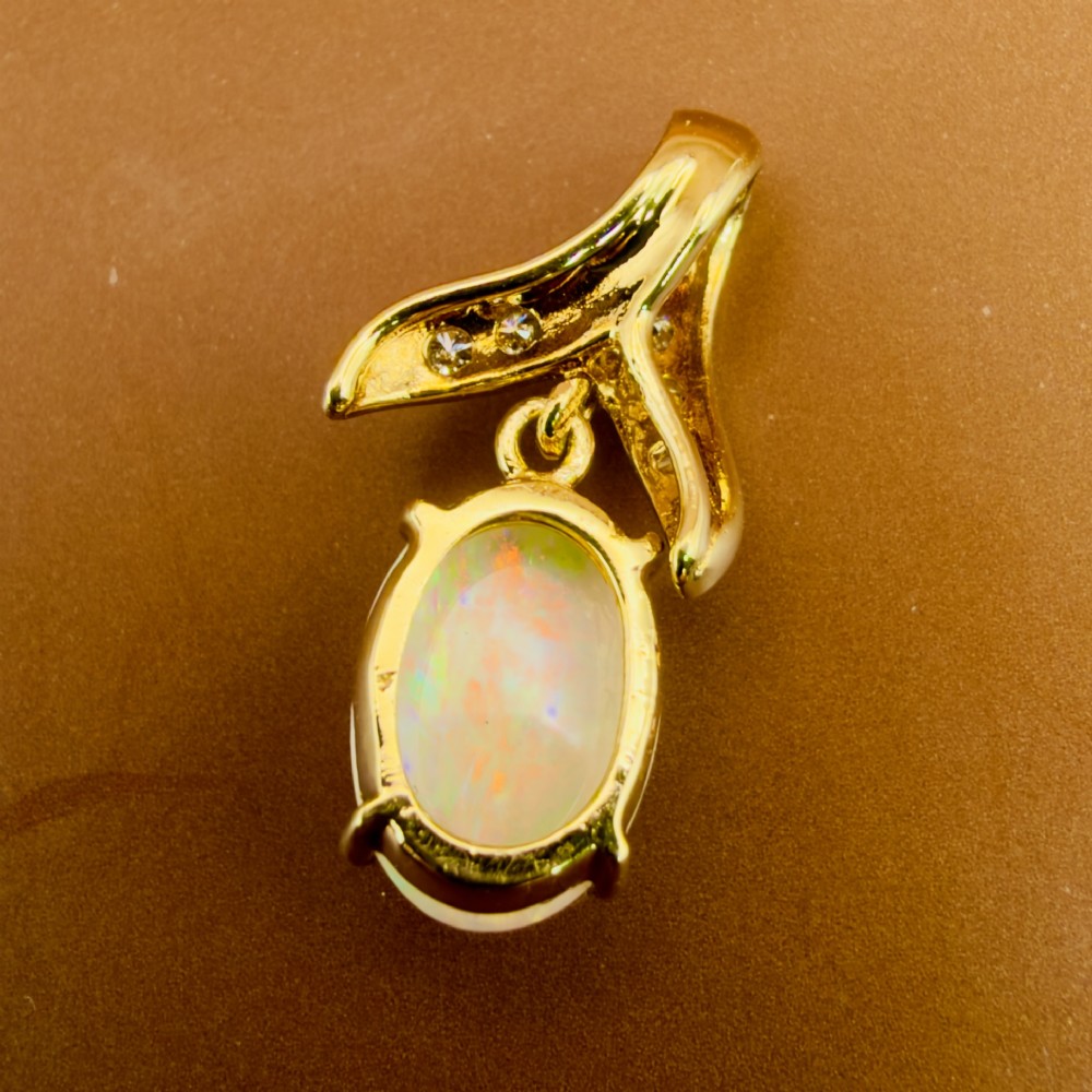 A 14ct yellow gold pendant featuring a claw-set cabochon opal hanging beneath a diamond-accented bail. View VII