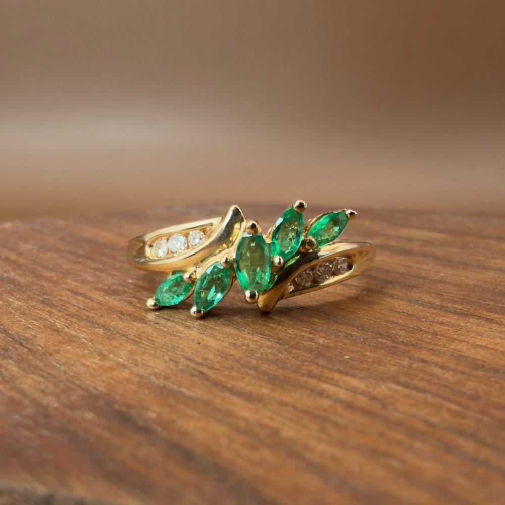 A 14ct yellow gold cluster ring set with five marquise-cut green emeralds flanked by channel-set diamonds. View VI
