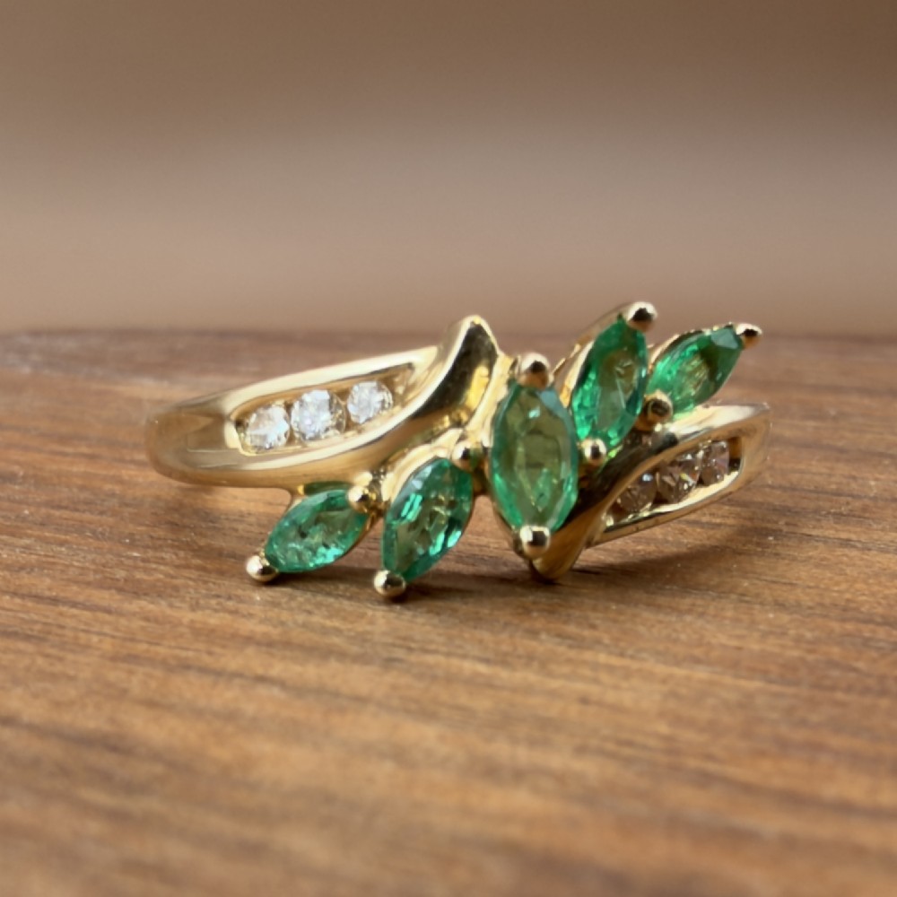 A 14ct yellow gold cluster ring set with five marquise-cut green emeralds flanked by channel-set diamonds. View VII