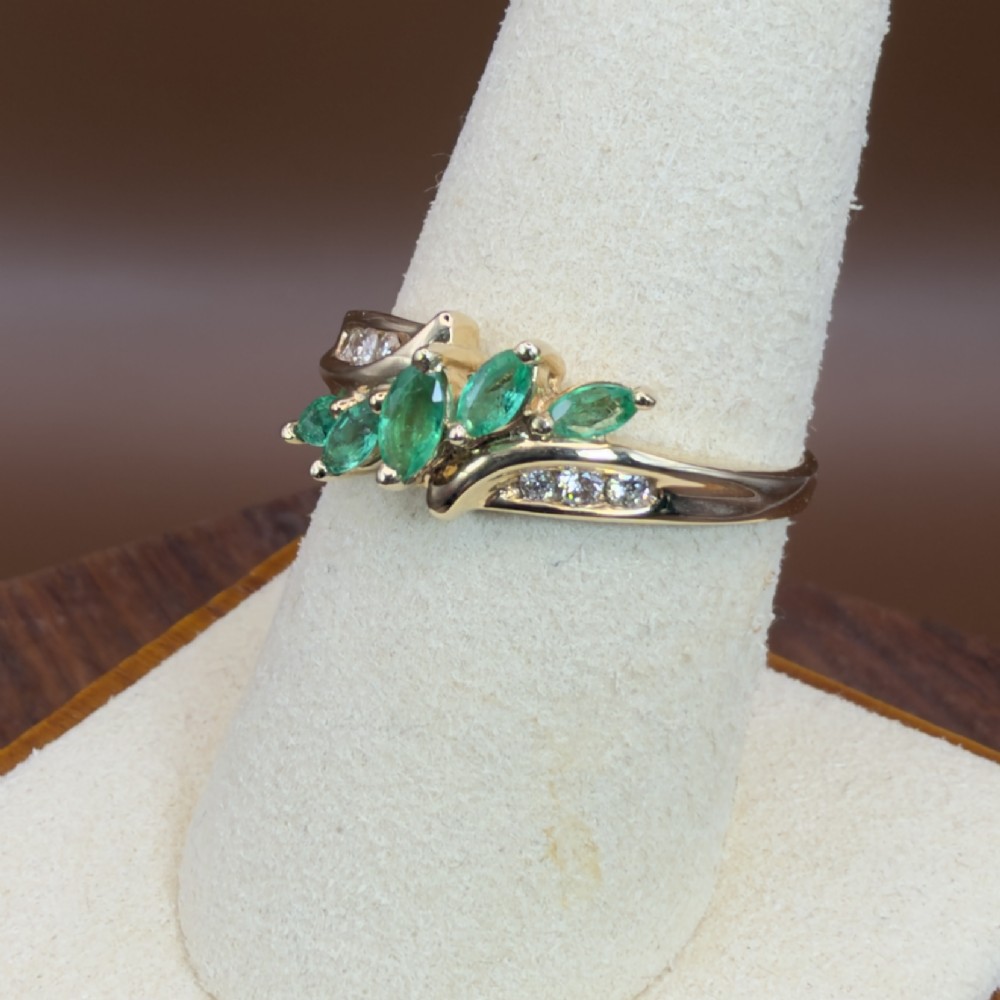 A 14ct yellow gold cluster ring set with five marquise-cut green emeralds flanked by channel-set diamonds. View IX