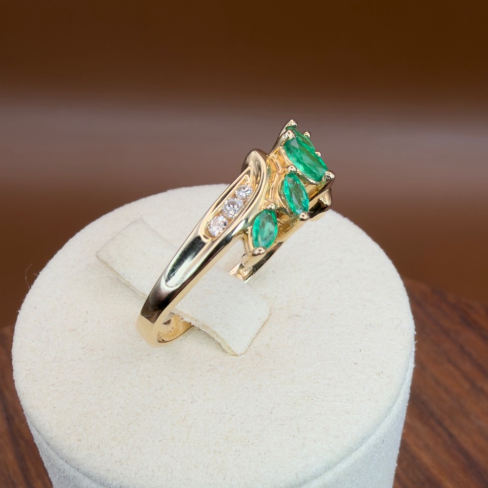 A 14ct yellow gold cluster ring set with five marquise-cut green emeralds flanked by channel-set diamonds. View XII