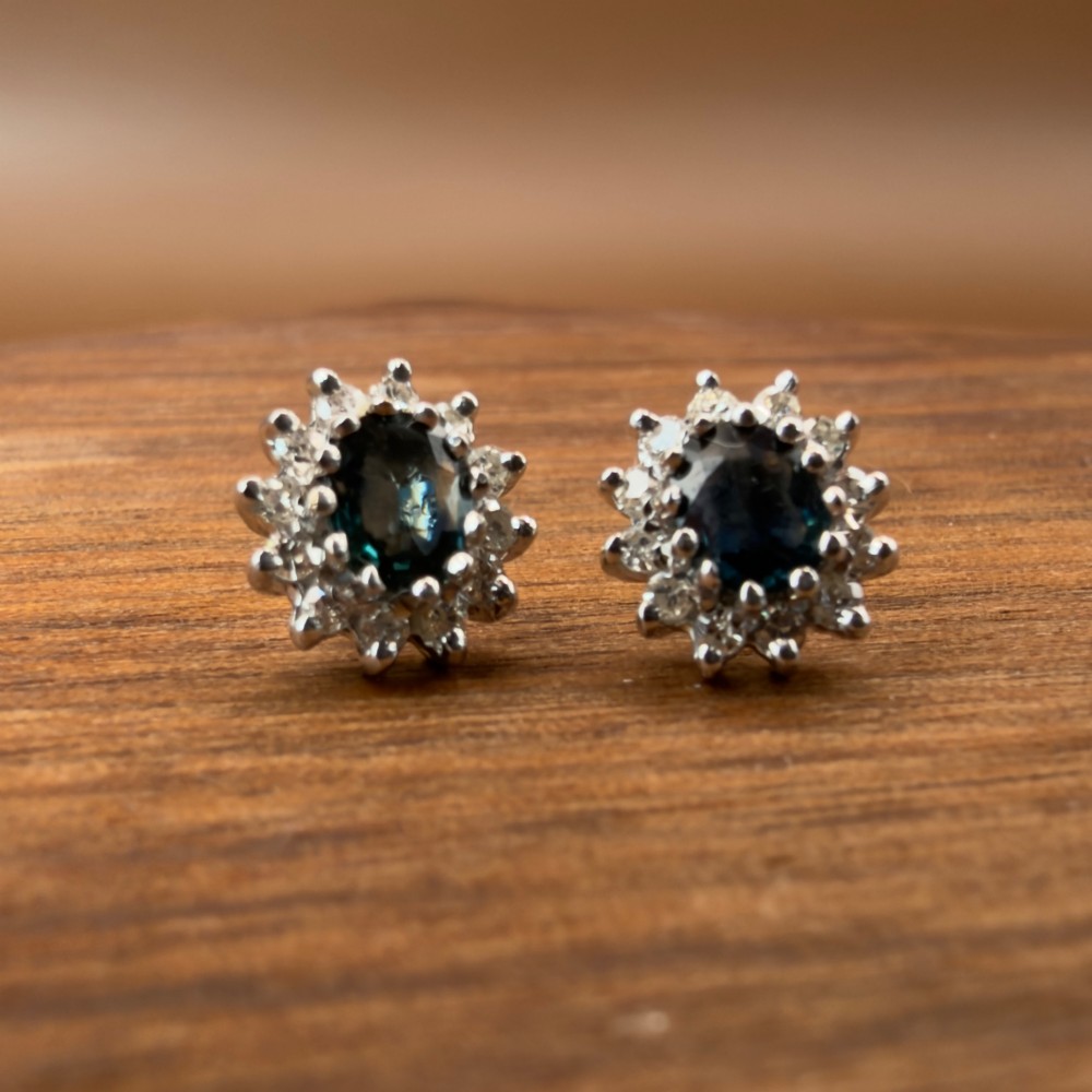 A pair of vintage 9ct gold stud earrings featuring oval deep blue sapphires surrounded by clusters of small diamonds. View V