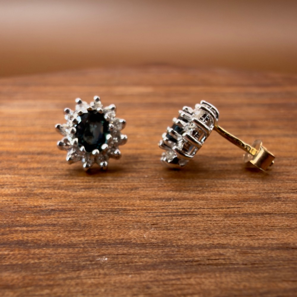 A pair of vintage 9ct gold stud earrings featuring oval deep blue sapphires surrounded by clusters of small diamonds. View VI