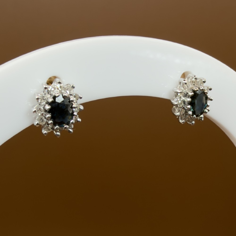 A pair of vintage 9ct gold stud earrings featuring oval deep blue sapphires surrounded by clusters of small diamonds. View VIII