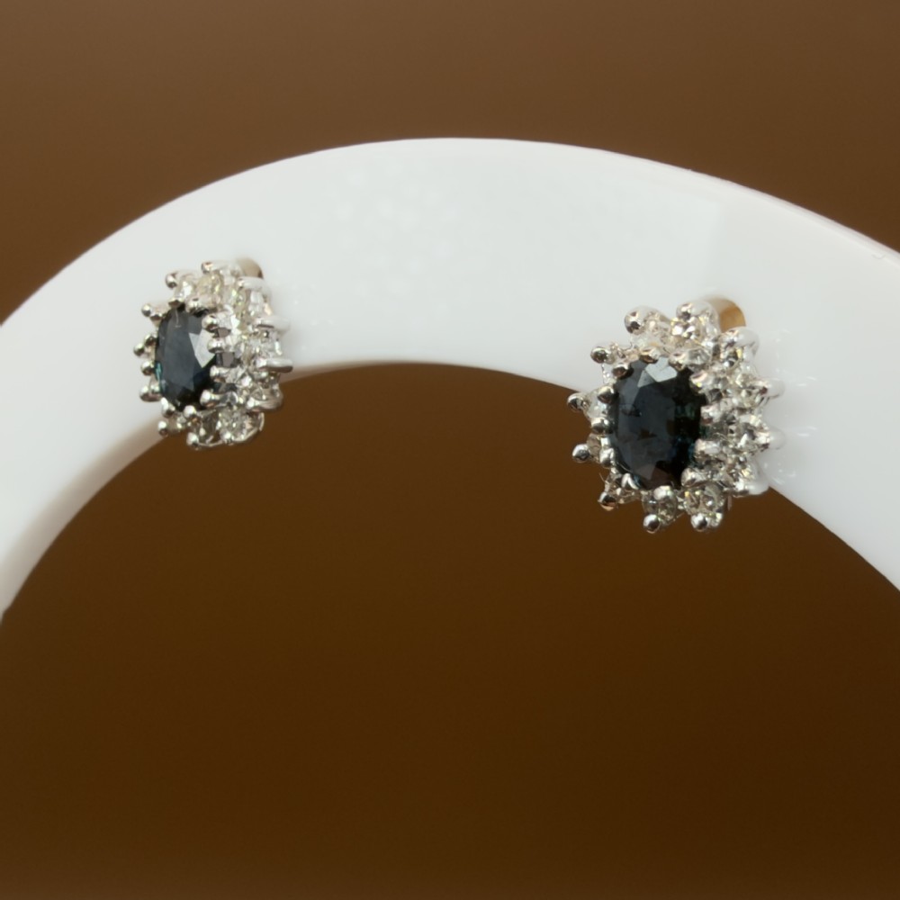 A pair of vintage 9ct gold stud earrings featuring oval deep blue sapphires surrounded by clusters of small diamonds. View IX