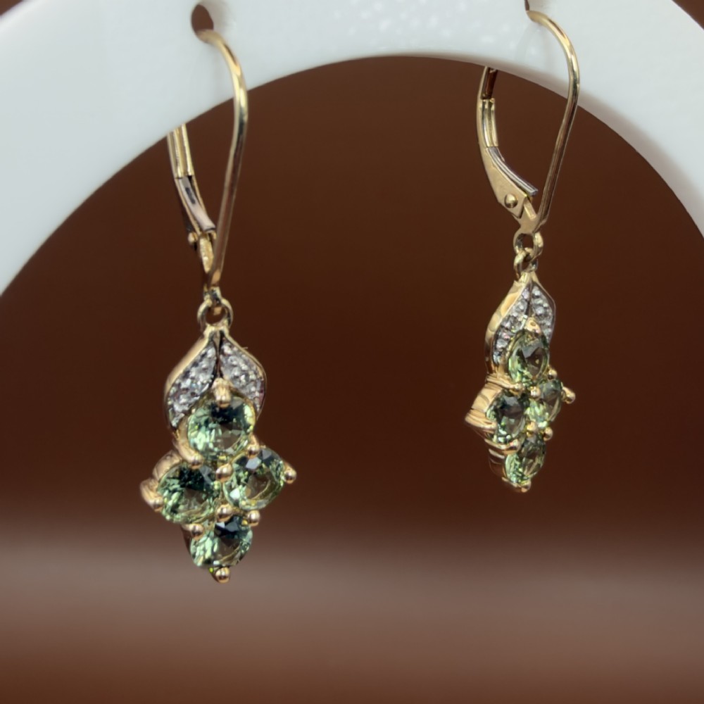 A pair of 9ct yellow gold drop earrings featuring a cluster of round-cut teal green sapphires suspended from hinge back hooks with diamond accent detail. View VI