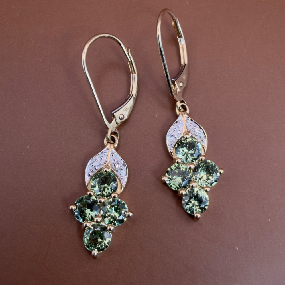 A pair of 9ct yellow gold drop earrings featuring a cluster of round-cut teal green sapphires suspended from hinge back hooks with diamond accent detail. View VIII