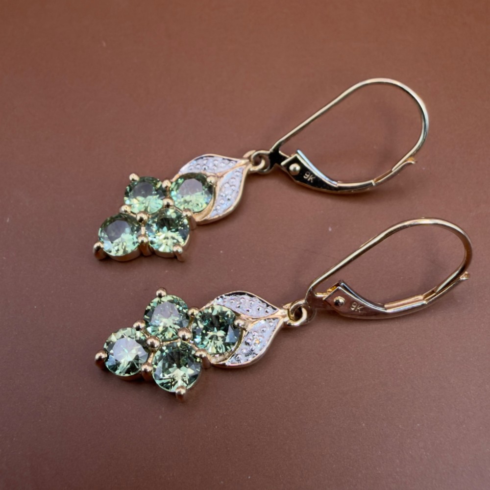 A pair of 9ct yellow gold drop earrings featuring a cluster of round-cut teal green sapphires suspended from hinge back hooks with diamond accent detail. View IX