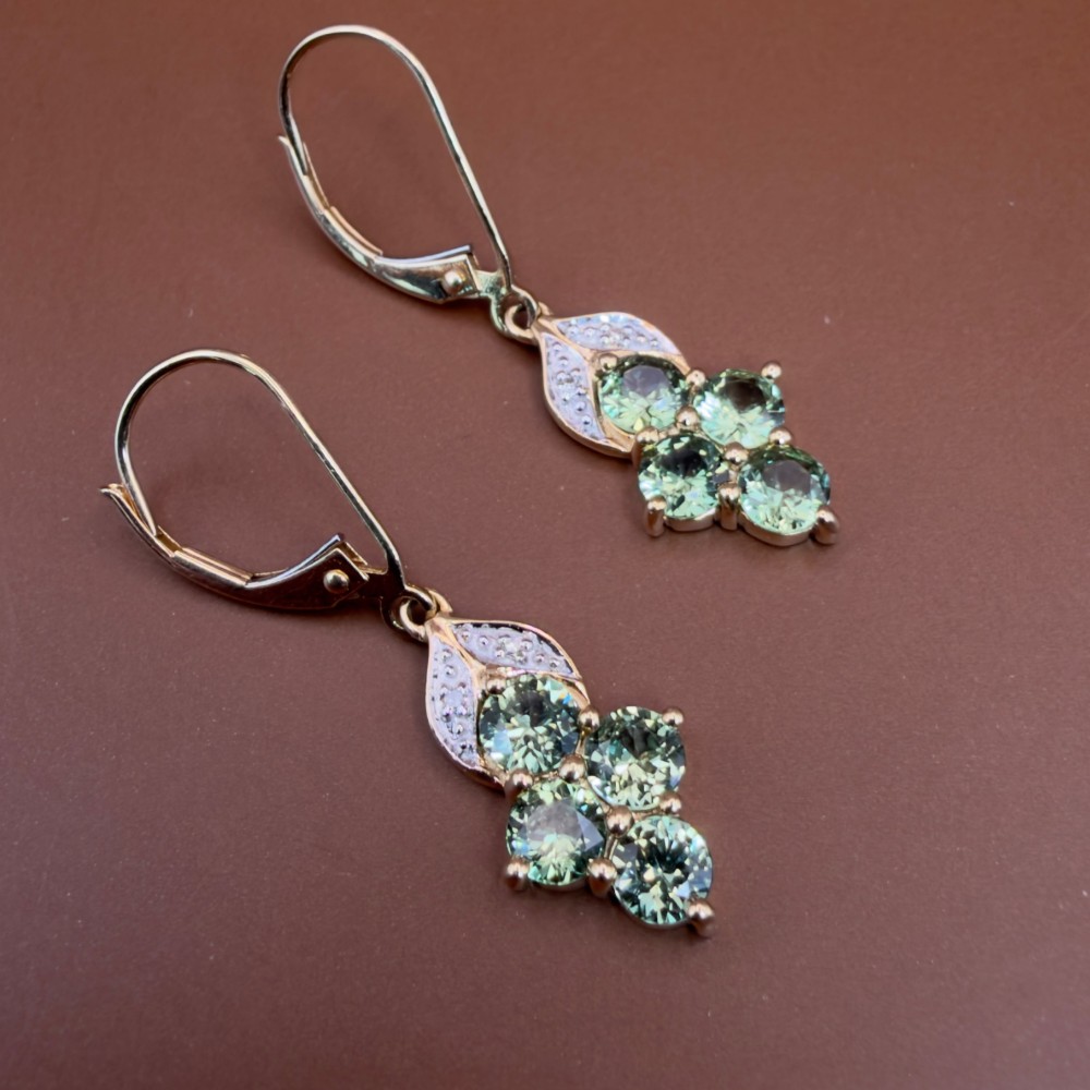 A pair of 9ct yellow gold drop earrings featuring a cluster of round-cut teal green sapphires suspended from hinge back hooks with diamond accent detail. View X