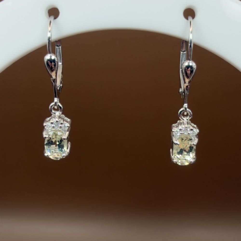 A pair of 9ct white gold drop earrings featuring oval cut pale green amethysts suspended beneath small diamond cluster accents with hinge back fastenings. View II