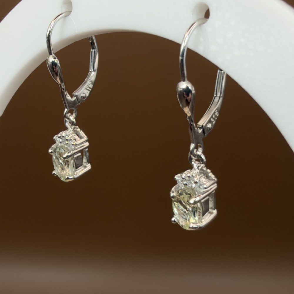 A pair of 9ct white gold drop earrings featuring oval cut pale green amethysts suspended beneath small diamond cluster accents with hinge back fastenings. View III