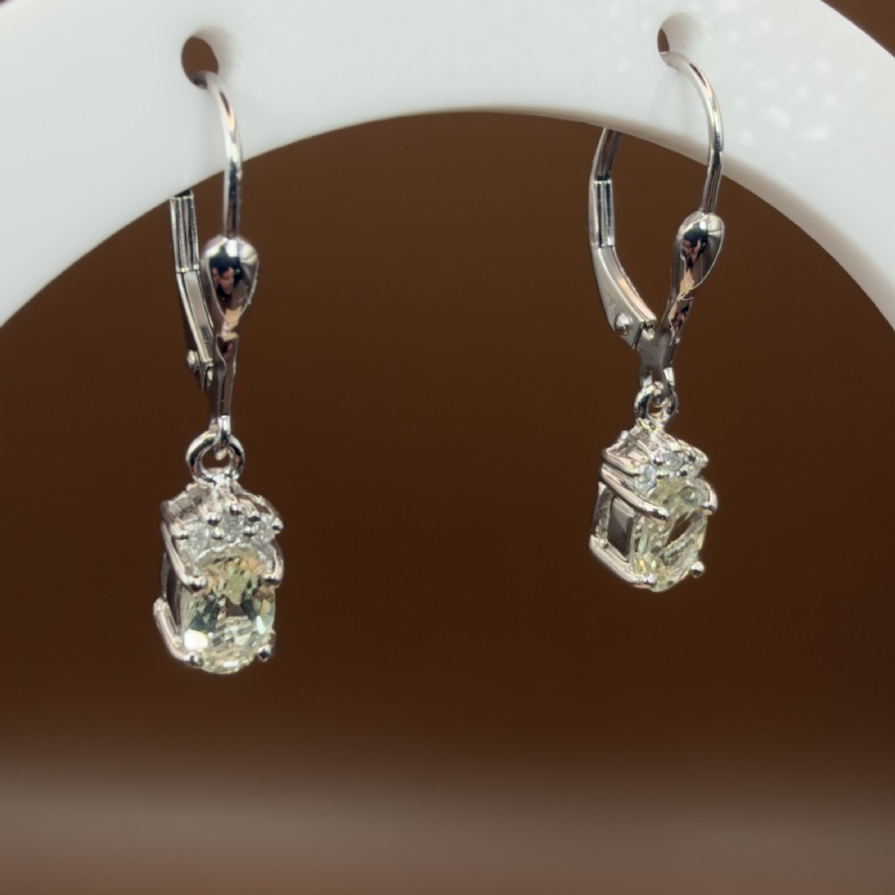 A pair of 9ct white gold drop earrings featuring oval cut pale green amethysts suspended beneath small diamond cluster accents with hinge back fastenings. View IV