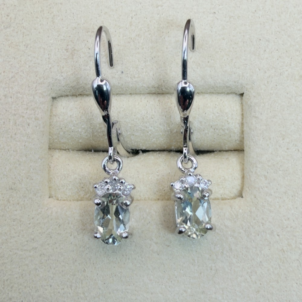 A pair of 9ct white gold drop earrings featuring oval cut pale green amethysts suspended beneath small diamond cluster accents with hinge back fastenings. View V