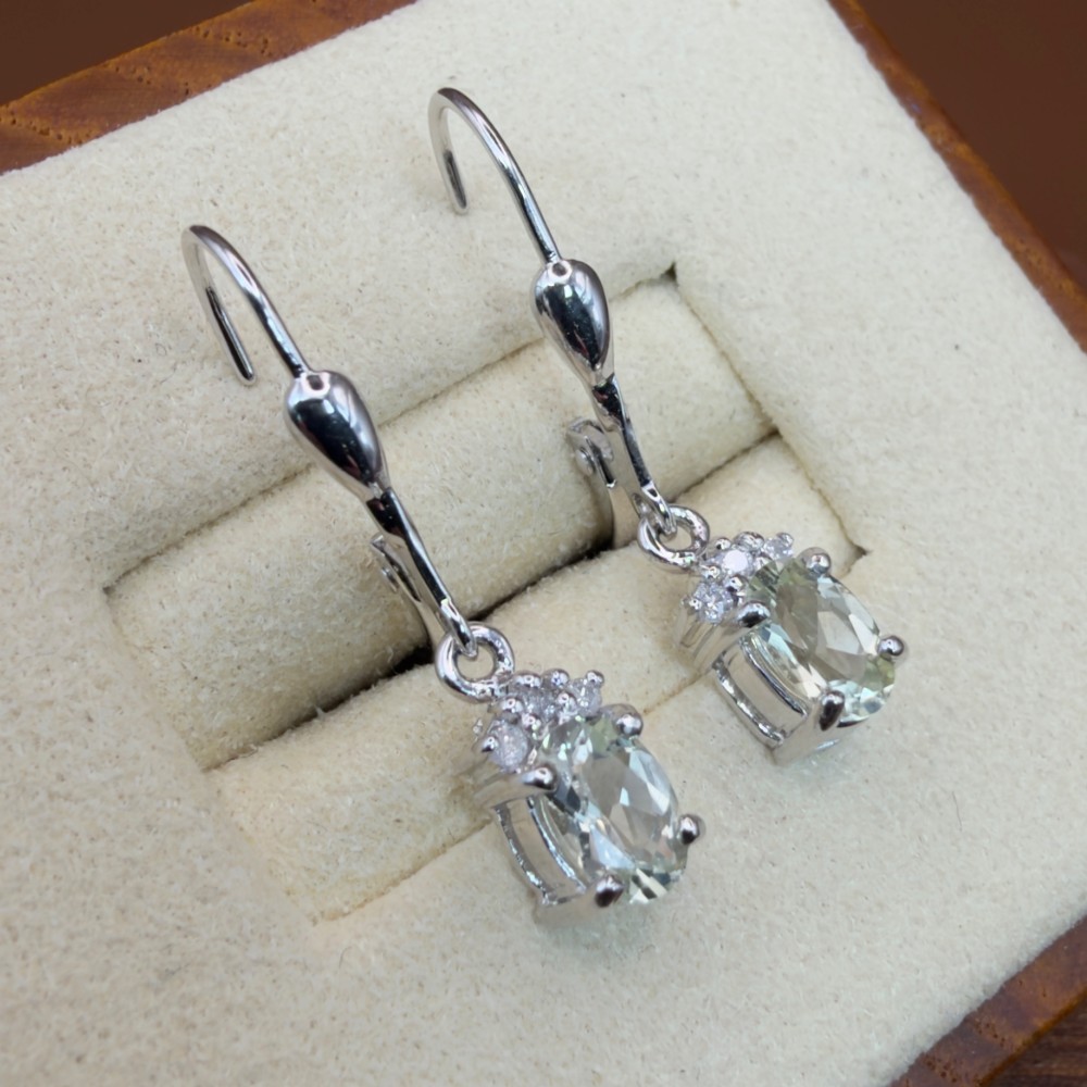 A pair of 9ct white gold drop earrings featuring oval cut pale green amethysts suspended beneath small diamond cluster accents with hinge back fastenings. View VII