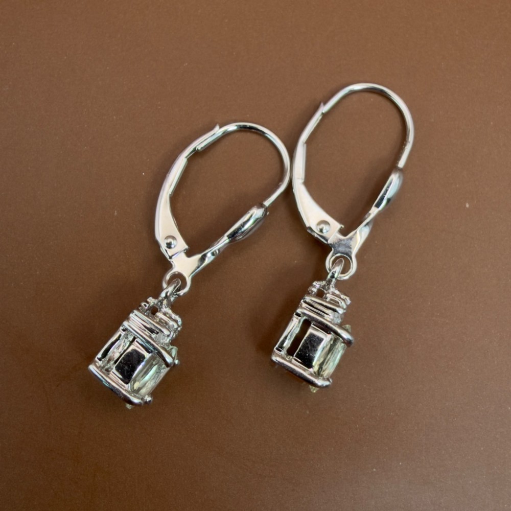 A pair of 9ct white gold drop earrings featuring oval cut pale green amethysts suspended beneath small diamond cluster accents with hinge back fastenings. View VIII