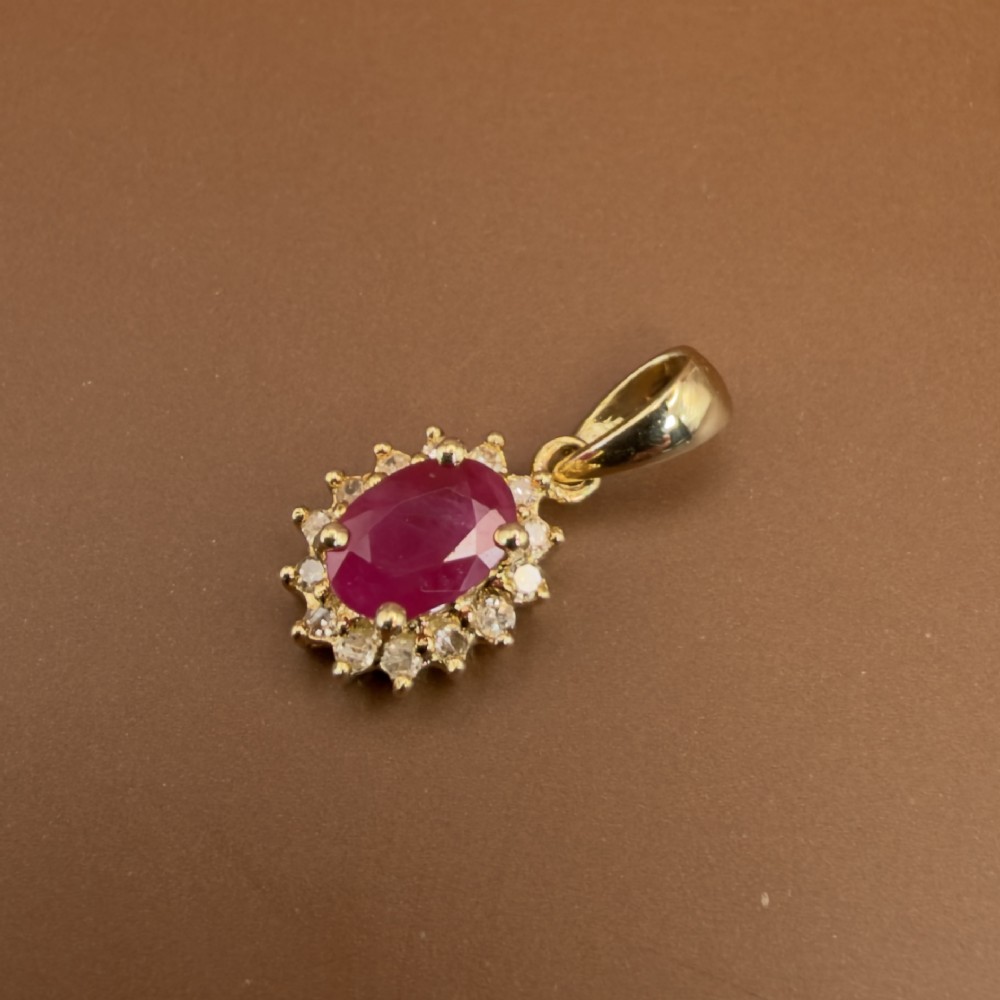 A 14ct yellow gold cluster pendant featuring an oval-cut red ruby framed by small round diamonds. View II