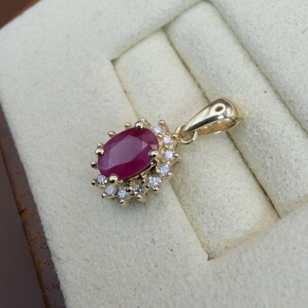 A 14ct yellow gold cluster pendant featuring an oval-cut red ruby framed by small round diamonds. View VI
