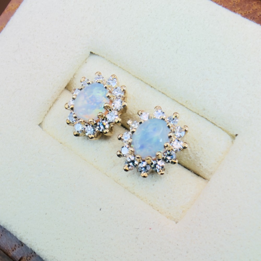 A pair of 9ct yellow gold stud earrings featuring central oval cabochon opals surrounded by a halo of small brilliant-cut diamonds. View IV