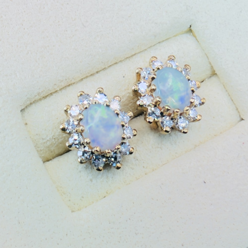 A pair of 9ct yellow gold stud earrings featuring central oval cabochon opals surrounded by a halo of small brilliant-cut diamonds. View II