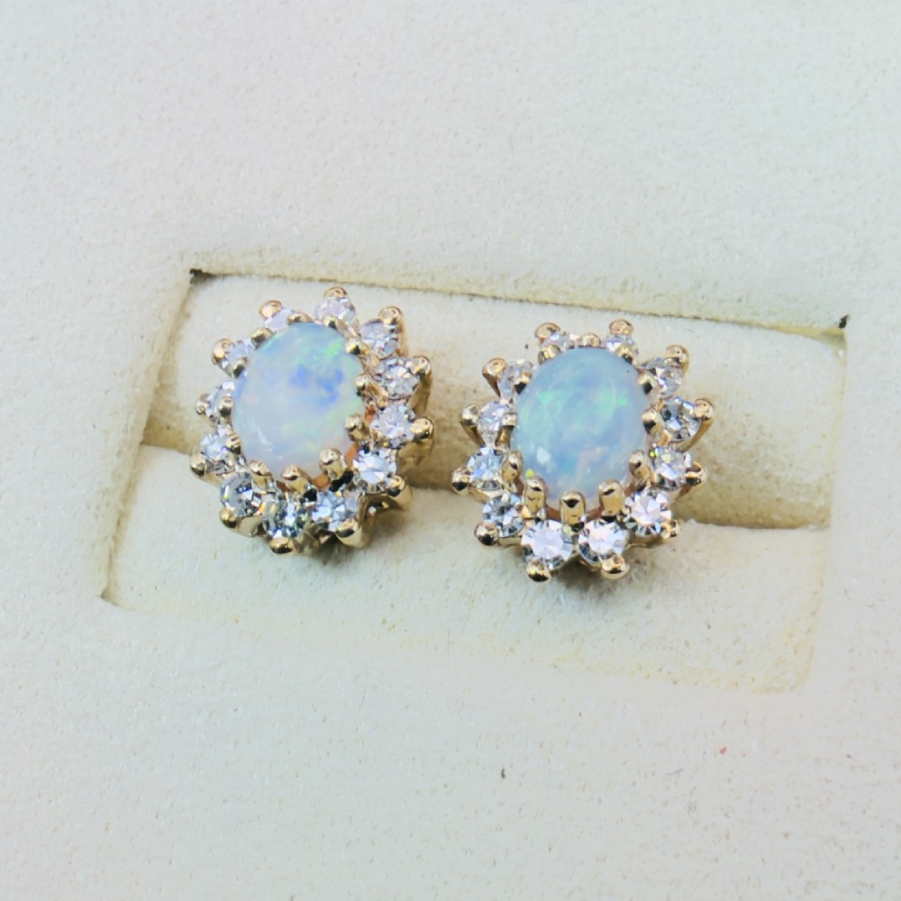 A pair of 9ct yellow gold stud earrings featuring central oval cabochon opals surrounded by a halo of small brilliant-cut diamonds. View V