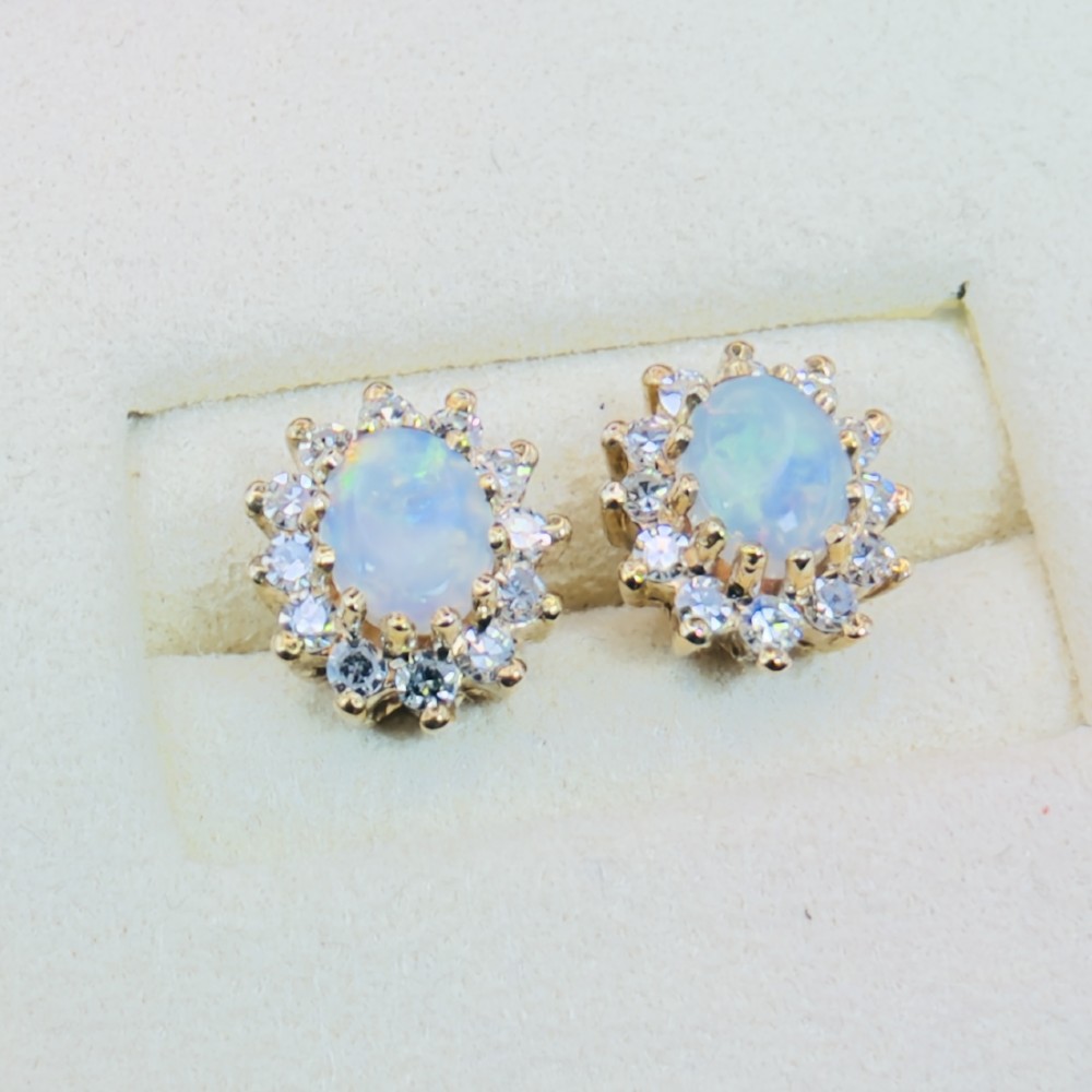 A pair of 9ct yellow gold stud earrings featuring central oval cabochon opals surrounded by a halo of small brilliant-cut diamonds. View VI