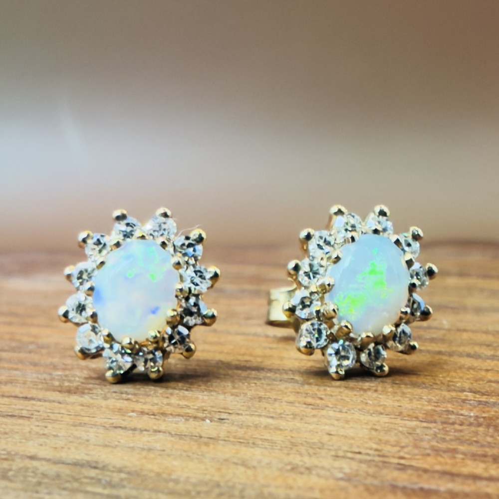 A pair of 9ct yellow gold stud earrings featuring central oval cabochon opals surrounded by a halo of small brilliant-cut diamonds. View VII