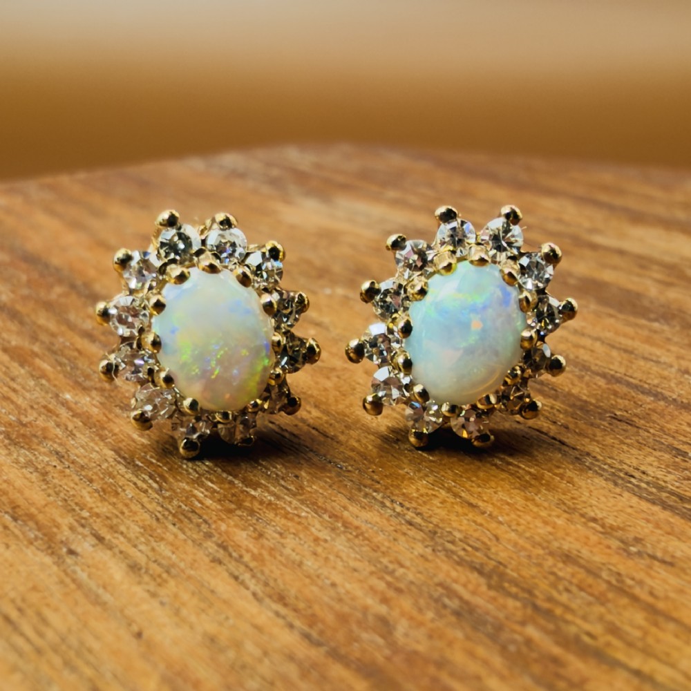 A pair of 9ct yellow gold stud earrings featuring central oval cabochon opals surrounded by a halo of small brilliant-cut diamonds. View X
