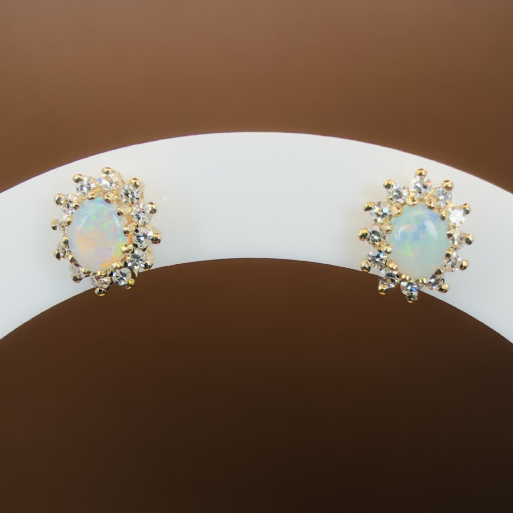 A pair of 9ct yellow gold stud earrings featuring central oval cabochon opals surrounded by a halo of small brilliant-cut diamonds. View XI
